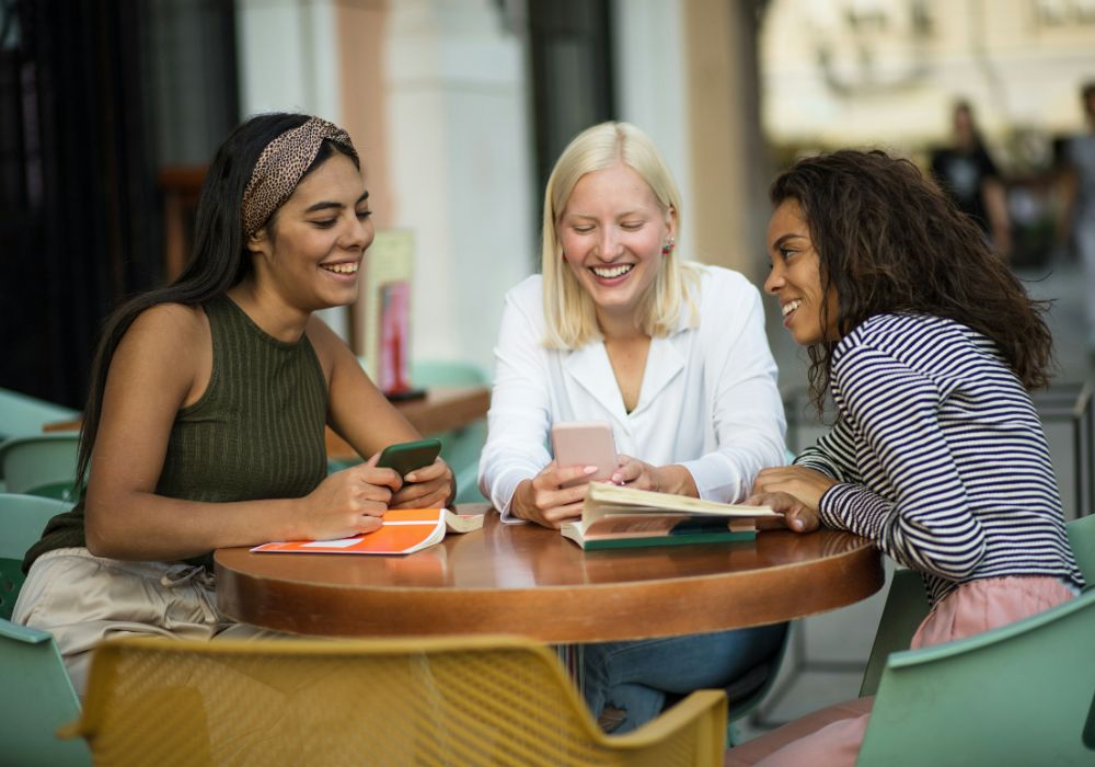 Three young women sitting at a table, each focused on their phones.